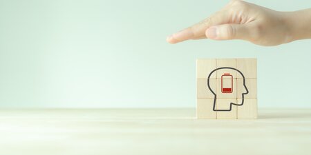Eine schützende Hand über Holzblöcken mit einem Symbol für psychische Gesundheit und niedrige Energie – ein Hinweis auf mentale Belastung am Arbeitsplatz. Eine schützende Hand über Holzblöcken mit einem Symbol für psychische Gesundheit und niedrige Energie – ein Hinweis auf mentale Belastung am Arbeitsplatz.